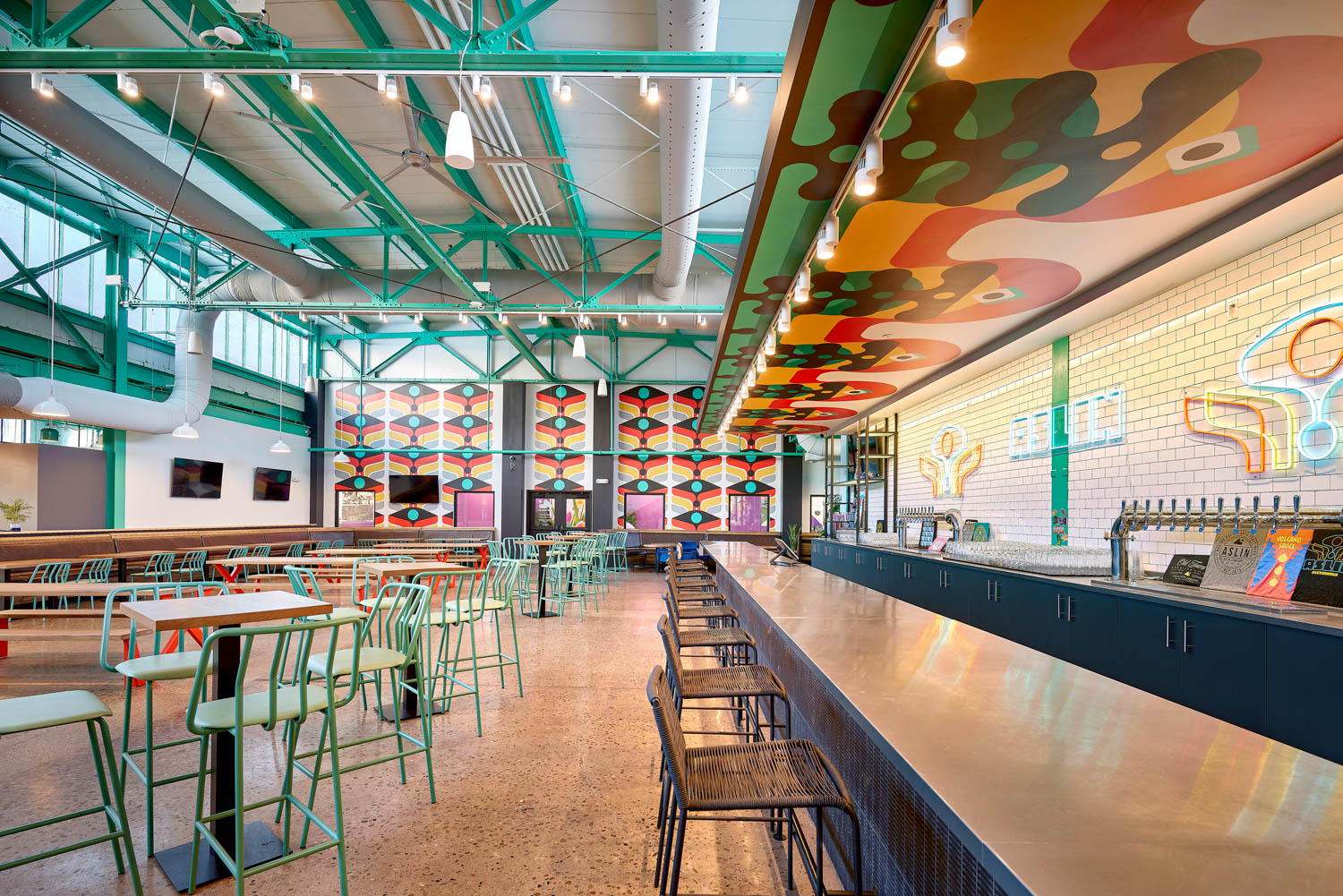 neon signs flash against white tiles at the bar of this brewery