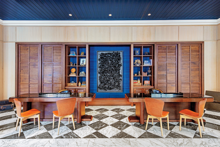 Wooden tables and chairs pop against a black and white checkered floor near a blue accent wall with shelving 