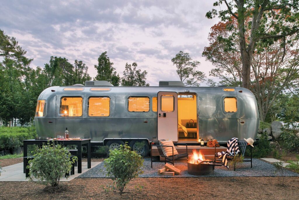 An inviting airstream trailer-turned-guest room in the woods of Cape Code with a fire pit. 