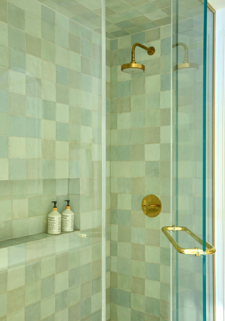 shower with green checkered tiling, bronze showerhead and glass door