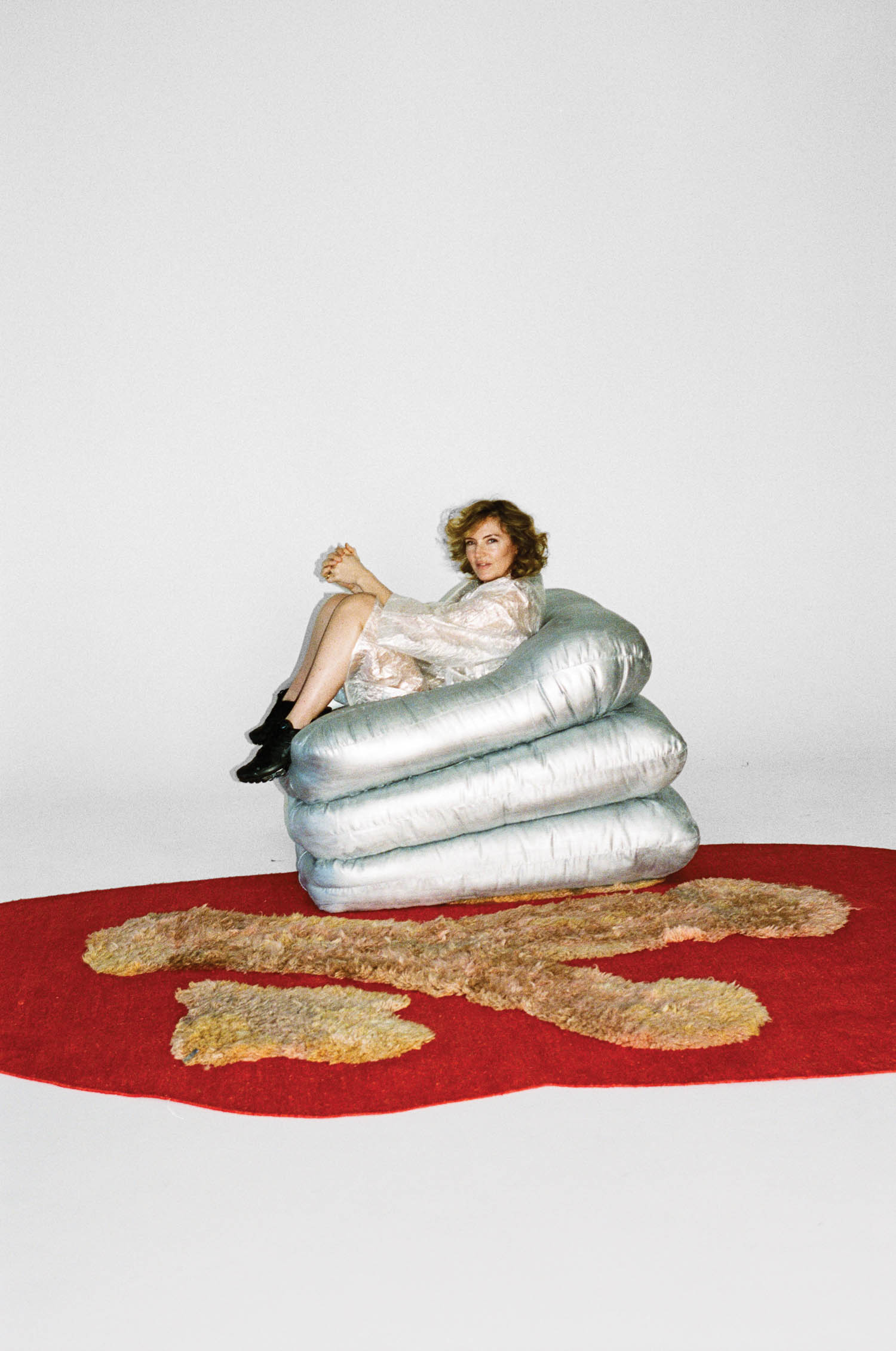 woman sitting on silver-white puffy chair on top of a red rug with yellow-brown patterns