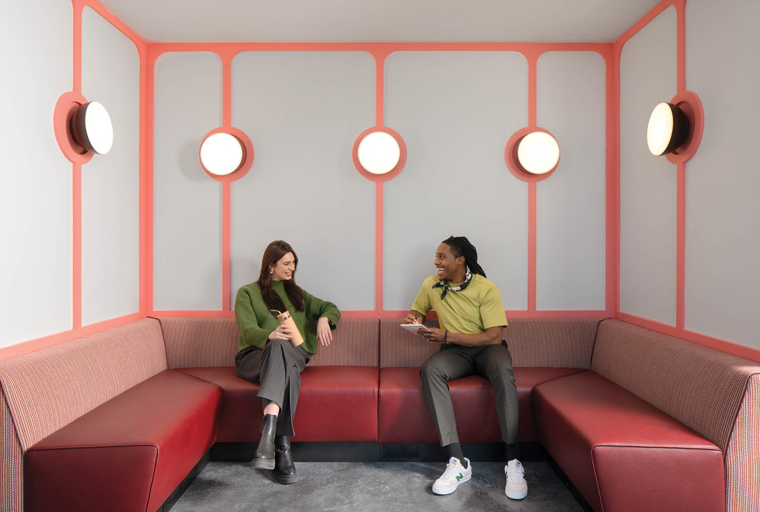 two people sitting in a long red booth area with lots of circular lights