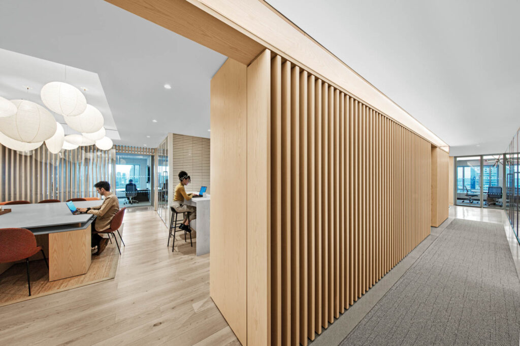 two people sitting in a room with worktables surrounded by pendant fixtures and white oak flooring