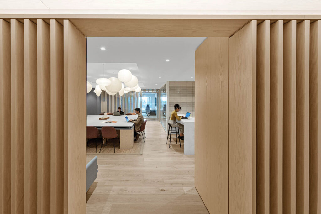 two people sitting in a room with worktables surrounded by pendant fixtures and white oak flooring