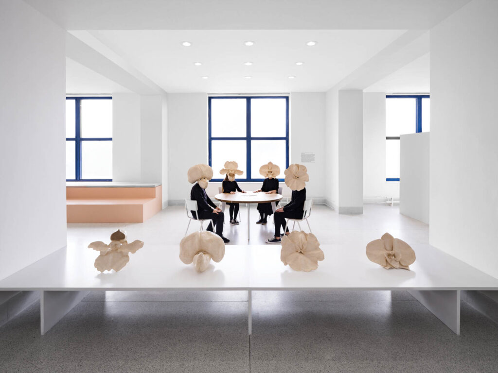 gallery visitors wearing glued-paper flower masks sitting at a table