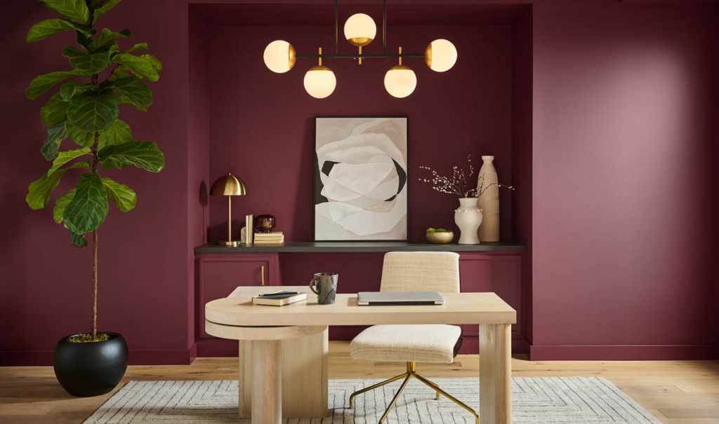 home office with dark red walls, wooden desk and chandelier